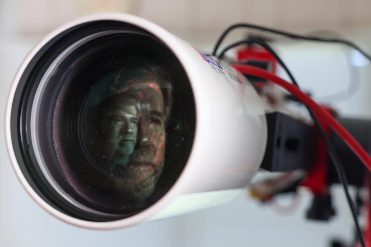 The bearded man's face is visible through the lens of the telescope. 