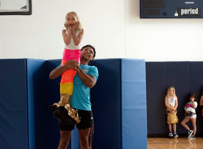 Stella Harper, 5, held by performance leader Anthony Trozolino, shows off her duct tape mermaid tail during the Funky Fashion show during Camp Palm Beach at the Mandel Recreation Center on July 10. 2024. Children ages 5 to 8 created a scene using trash bags and a funnel.  tape.  The last day of the camp is July 26, 2024.